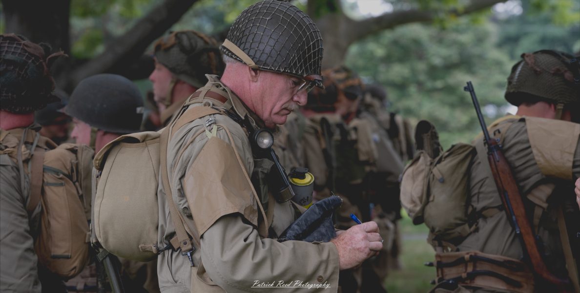 An army officer inspecting his troops, walking confidently among the ranks. His posture is authoritative, and he observes the soldiers closely, reflecting leadership and the importance of maintaining discipline and readiness within the unit.